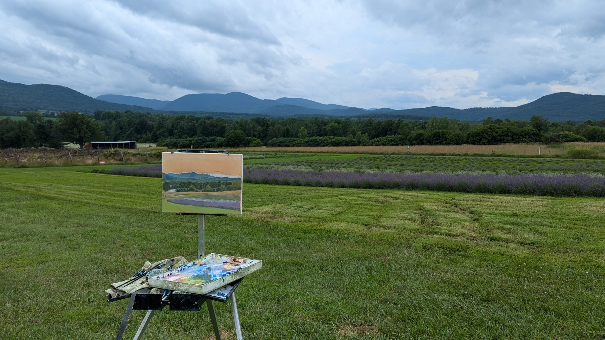 Plein air painting at a landscape with mountains, fields and clouds